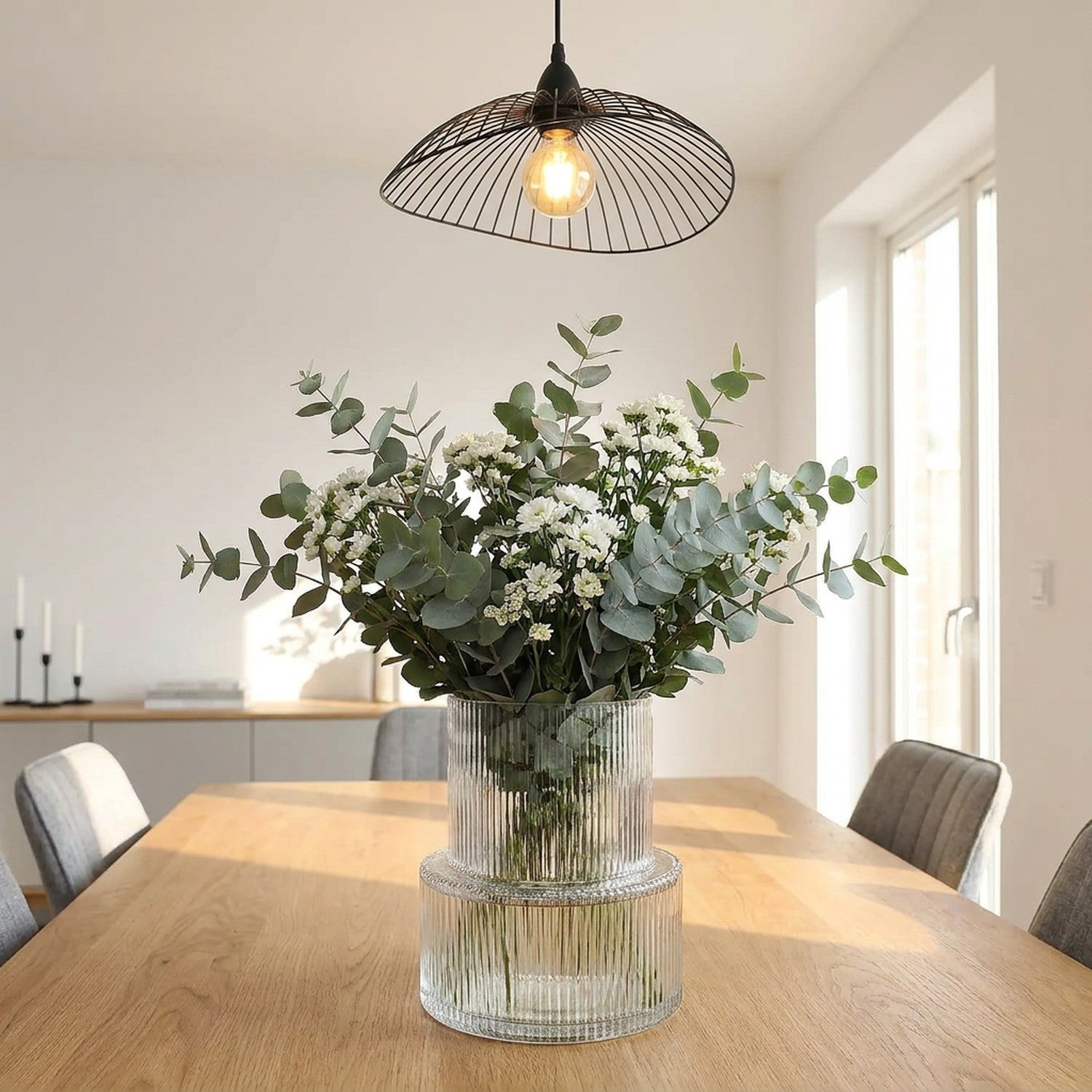 Vase en verre rayé avec bouquet sur table à manger sous un luminaire suspendu