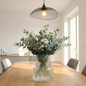 Vase en verre rayé avec bouquet sur table à manger sous un luminaire suspendu