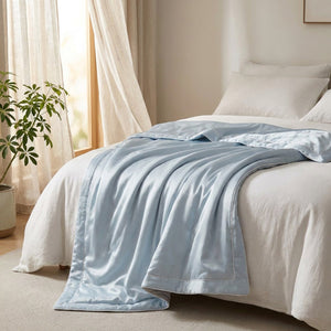 Couette d'été bleue en soie glacée drapée au pied d'un lit près d'une fenêtre lumineuse