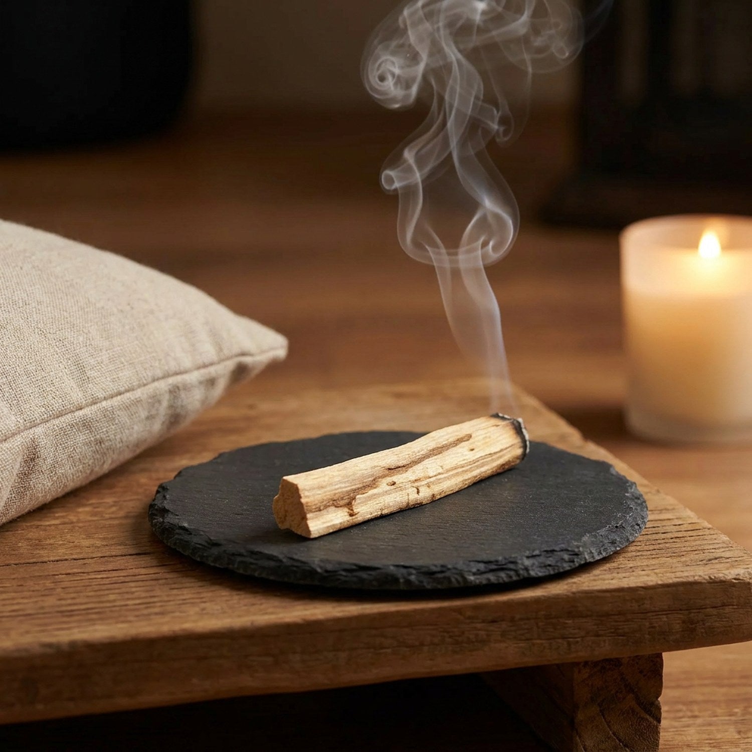 Bâtonnet de Palo Santo qui se consume sur une ardoise près d'un coussin en lin