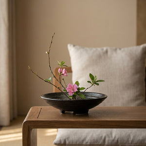 Vase japonais en céramique noire avec arrangement floral sur une table basse