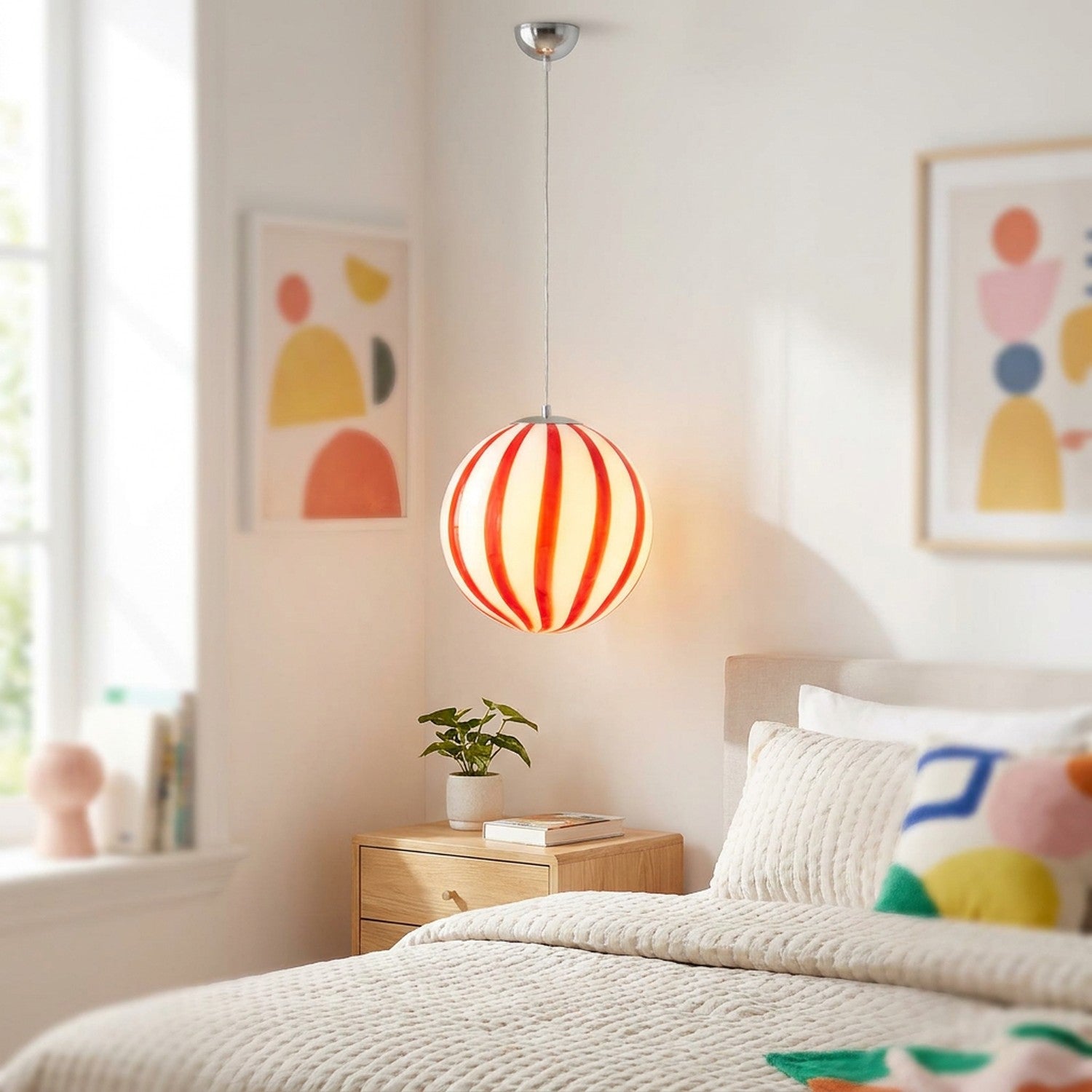 Suspension boule en verre rouge à rayures verticales allumée dans une chambre lumineuse et gaie