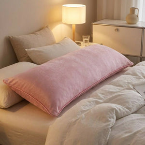 Taie d'oreiller longue rose sur un lit avec lampe de chevet allumée