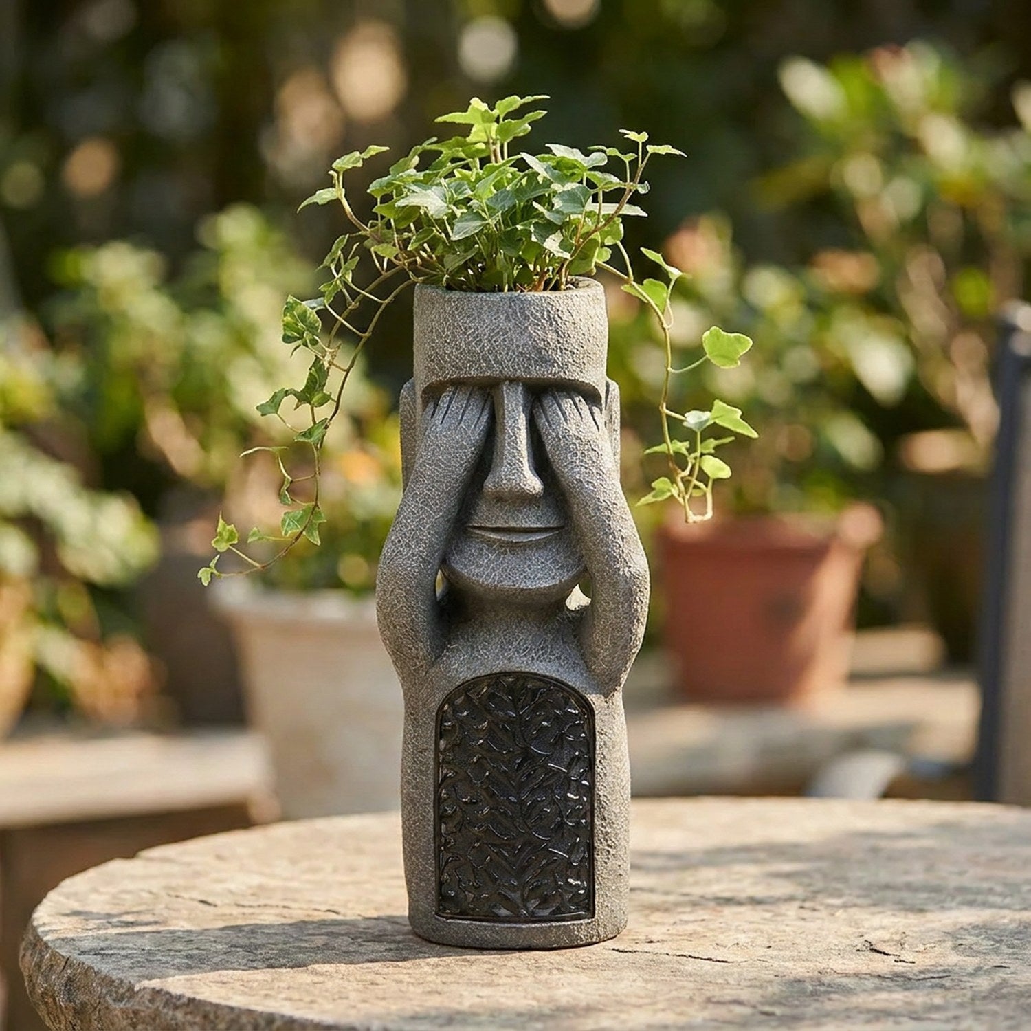 Statue Moai utilisée en cache-pot avec une plante retombante sur une table de jardin en pierre