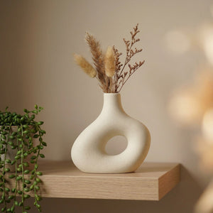 Petit vase en céramique donut blanc cassé sur une étagère avec fleurs séchées