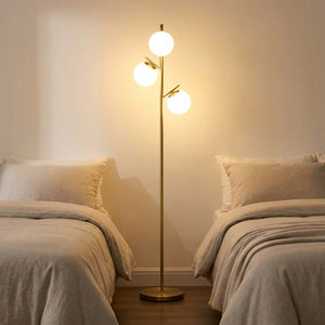 Lampadaire doré 3 globes allumé dans une chambre cosy entre deux lits