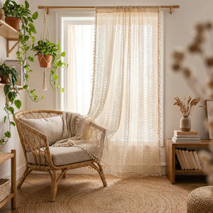 Rideau voilage boho en dentelle beige suspendu dans un salon cosy avec fauteuil en rotin