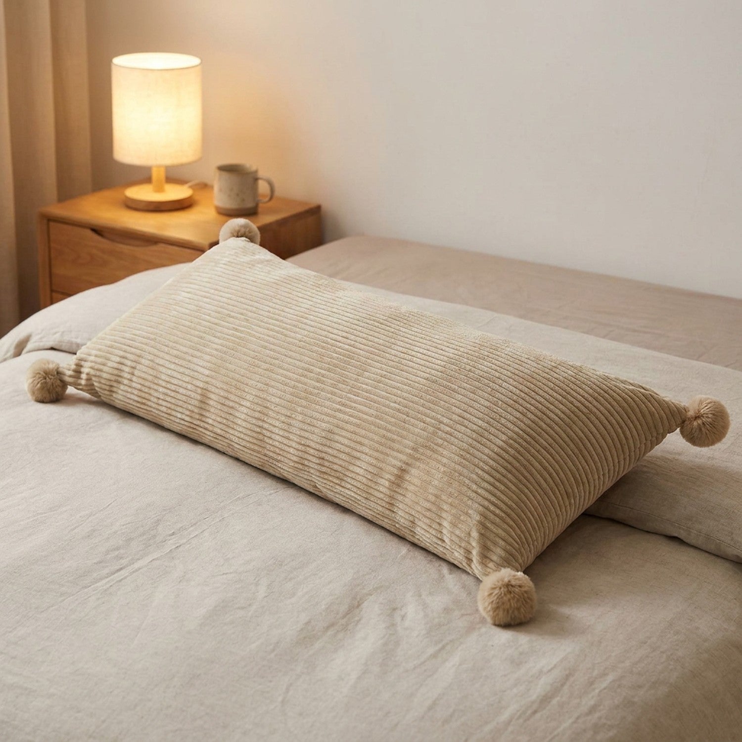 Coussin long en velours côtelé beige sur un lit près d'une lampe de chevet