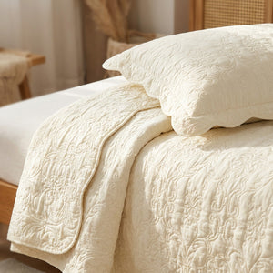 Gros plan sur la texture matelassee en relief du couvre-lit ivoire et sa taie assortie