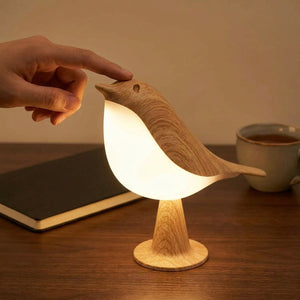 Main effleurant la tête de la lampe oiseau sur un bureau en bois le soir