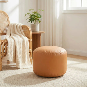 Pouf en simili cuir caramel dans un coin lecture avec fauteuil en rotin et plaid
