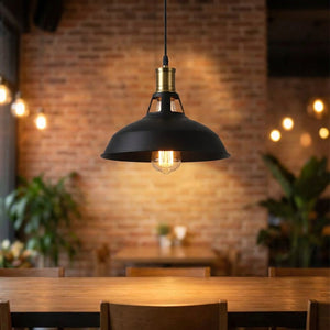 Suspension industrielle noire allumée au-dessus d'une table contre un mur de briques
