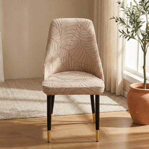 Chaise habillée de la housse beige au motif feuilles dans un coin salon lumineux avec une plante