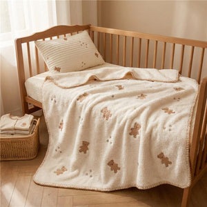Couverture bébé oursons étalée sur un lit à barreaux avec coussin assorti