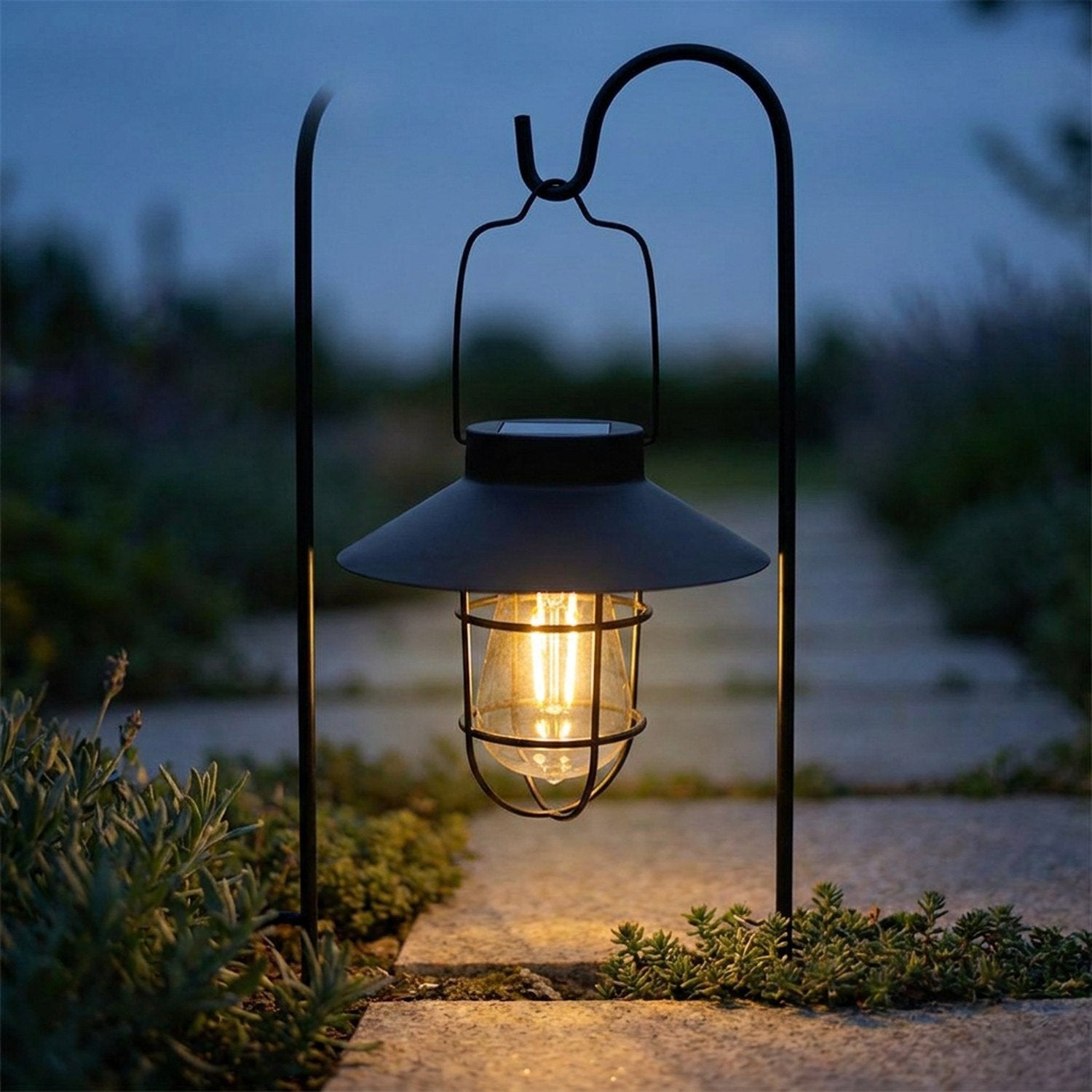 Lanterne solaire noire allumée sur un piquet le long d'une allée de jardin au crépuscule