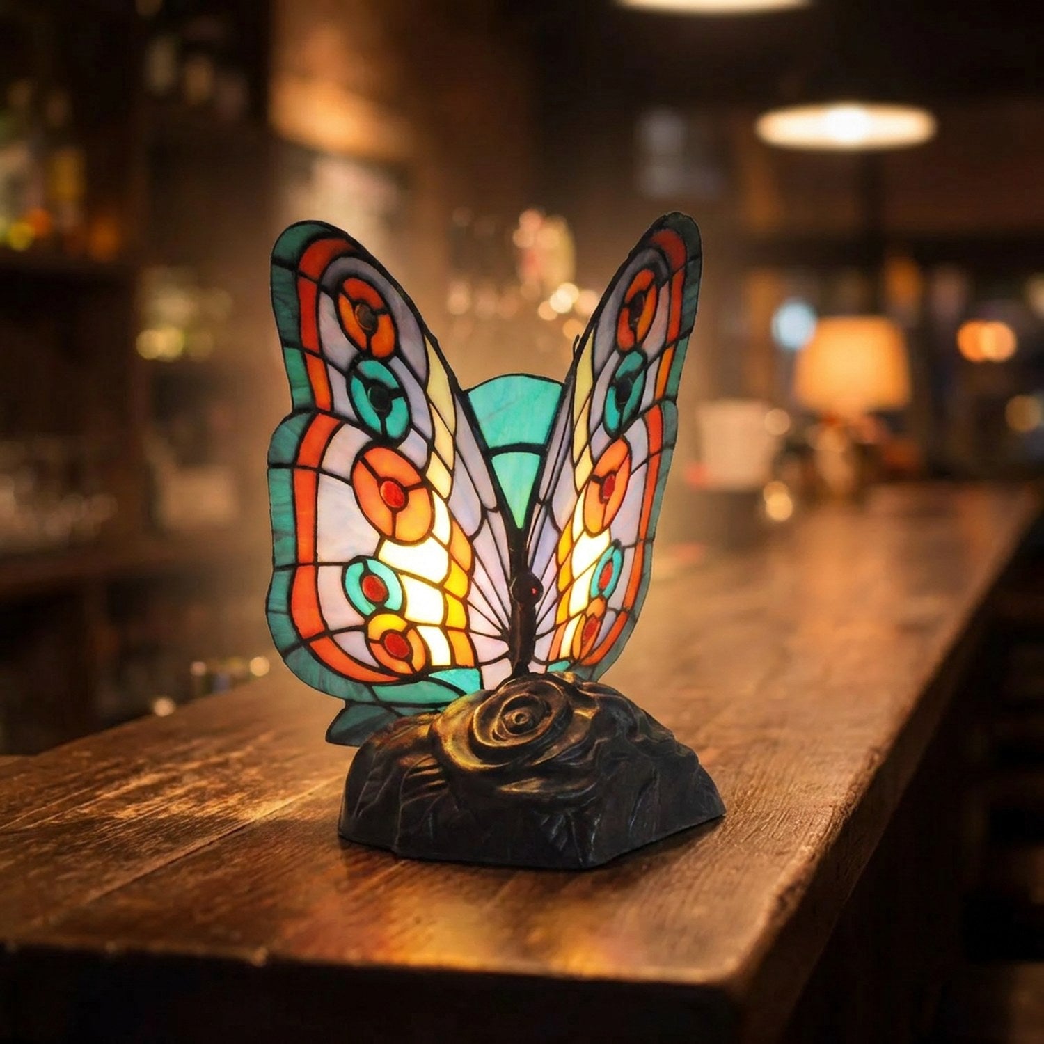 Lampe papillon en vitrail turquoise allumée sur un comptoir en bois dans une ambiance chaleureuse