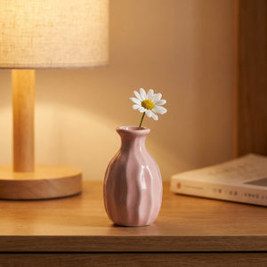 Vase soliflore en céramique côtelé rose avec une marguerite près d'une lampe
