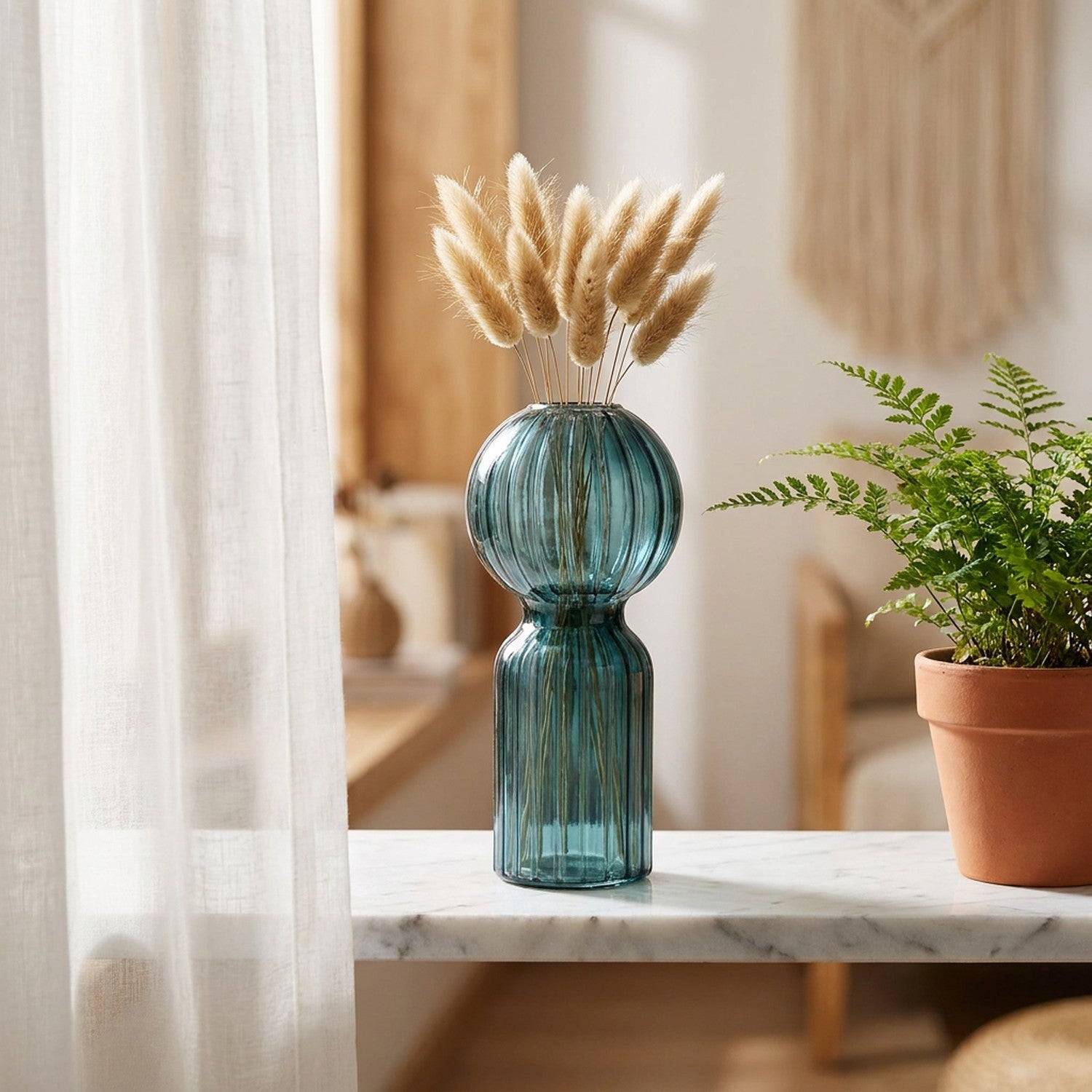 Vase en verre nervuré bleu sur une étagère en marbre près d une fougère