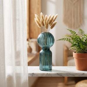 Vase en verre nervuré bleu sur une étagère en marbre près d une fougère