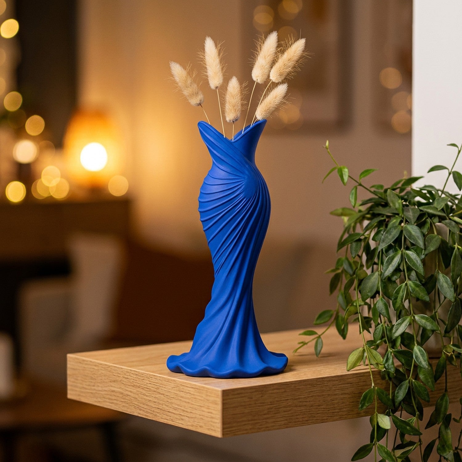 Vase bleu en forme de robe sur une étagère en bois près d'une plante