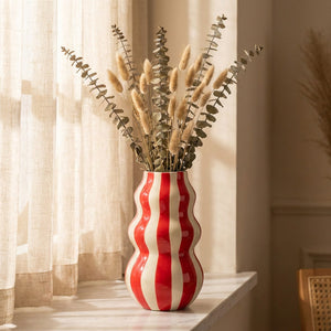 Grand vase rayé rouge aux courbes ondulées avec eucalyptus sur une étagère en marbre