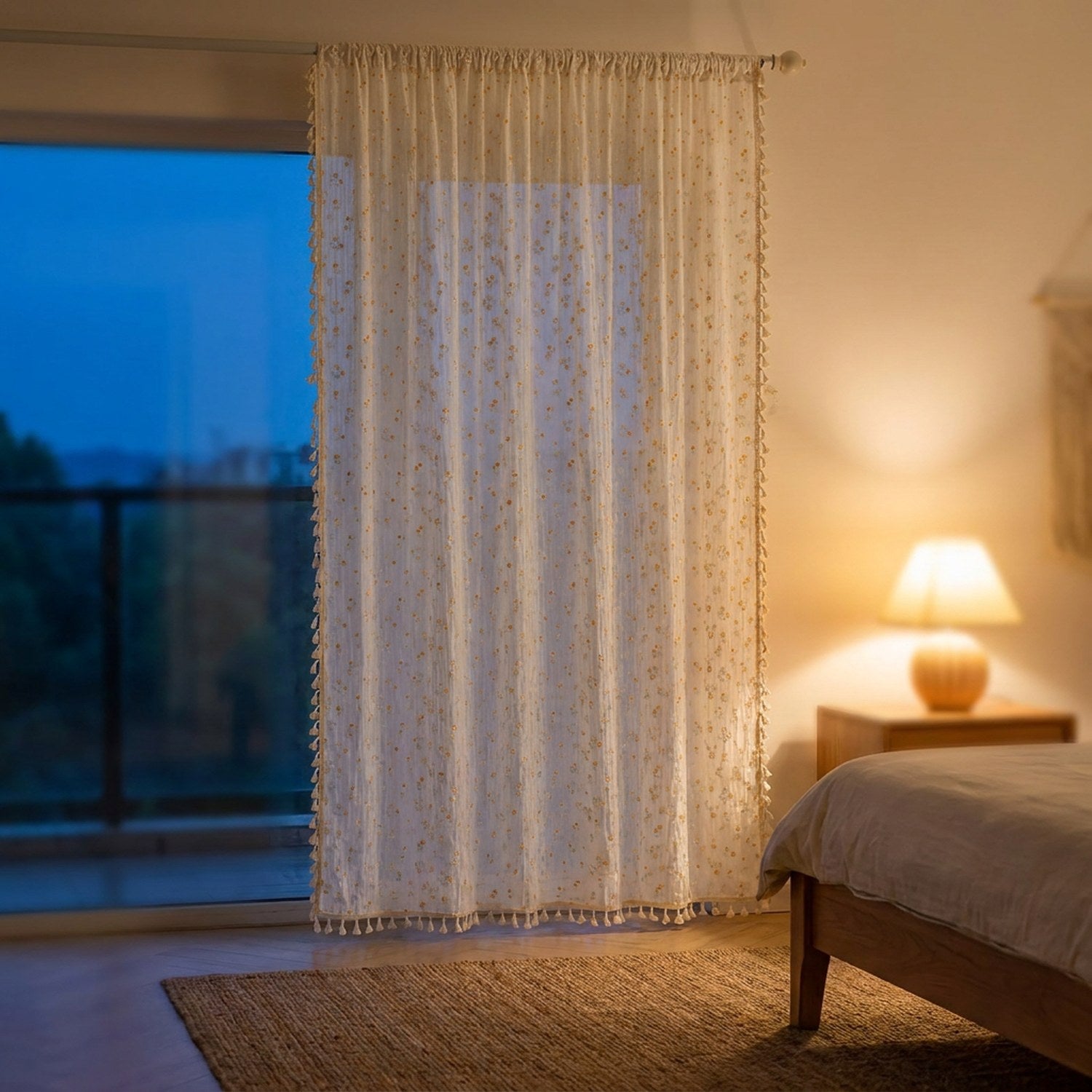 Rideau bohème fleuri suspendu devant une baie vitrée en soirée avec lampe allumée