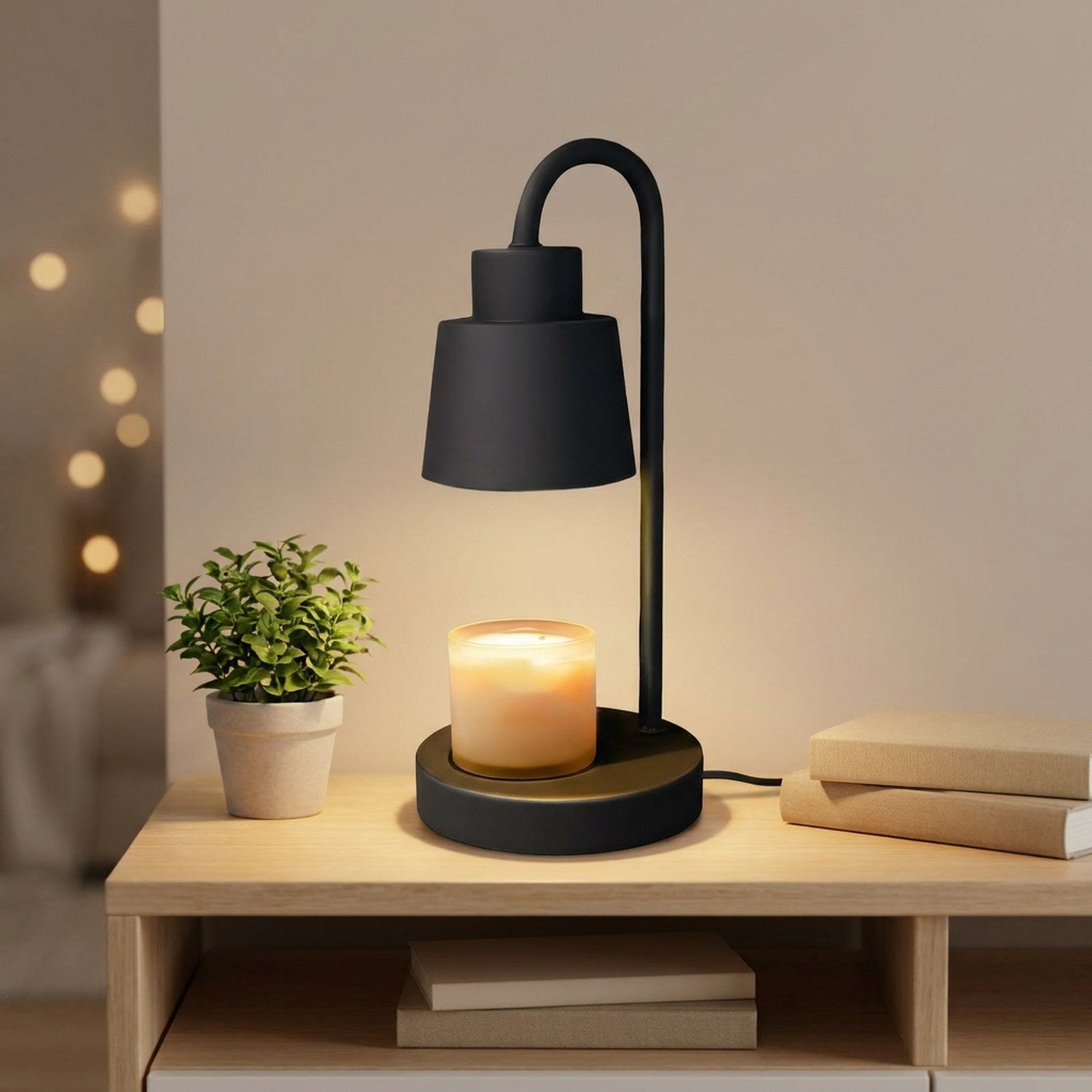 Lampe chauffe-bougie noire sur une table de chevet avec une plante verte et des livres