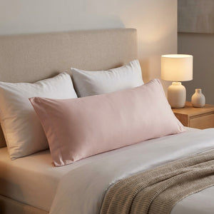 Taie d'oreiller longue rose habillant un traversin sur un lit moderne avec lampe de chevet