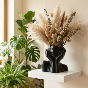 Vase noir céramique visage avec fleurs séchées sur étagère murale plantes arrière-plan