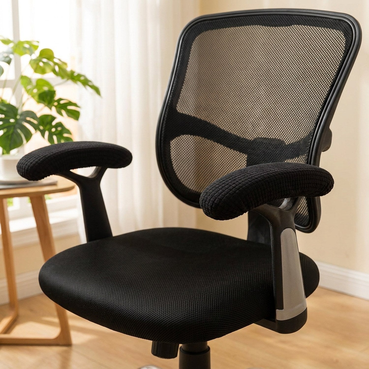 Fauteuil de bureau avec ses housses d'accoudoir noires dans un coin bureau lumineux et chaleureux