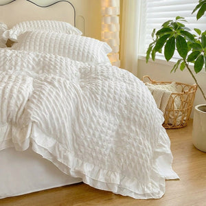 Parure de lit blanche à volants dans une chambre scandinave avec panier en rotin