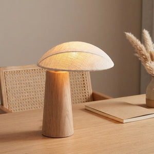 Lampe champignon en bois allumée sur un bureau à côté d'une chaise en rotin