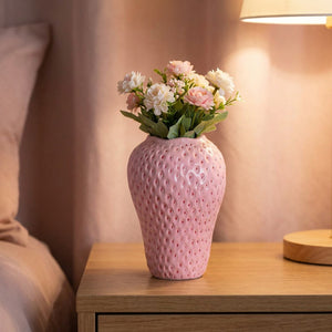 Vase rose en forme de fraise sur une table de chevet avec une lampe à la lumière douce