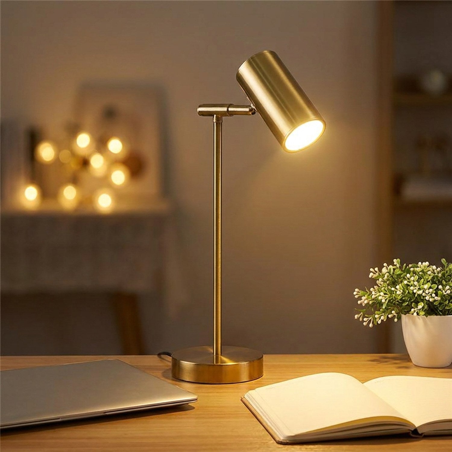 Lampe de bureau dorée allumée sur un bureau de travail avec ordinateur et carnet