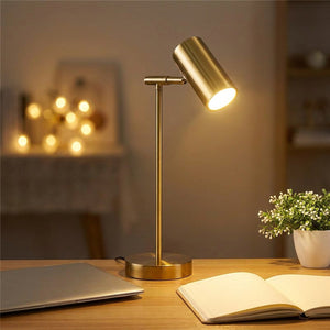 Lampe de bureau dorée allumée sur un bureau de travail avec ordinateur et carnet