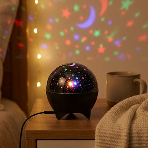 Veilleuse projecteur en dôme noir posée sur une table de chevet près d'une tasse projetant des étoiles sur le mur