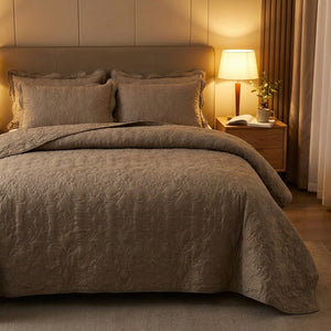 Couvre-lit matelasse taupe sur un lit dans une chambre cosy eclairee par une lampe de chevet