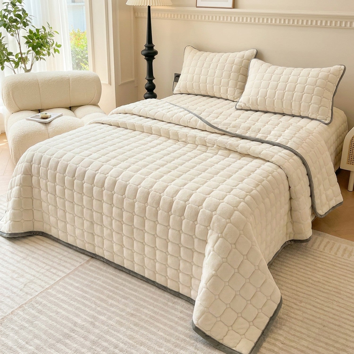 Couvre-lit matelassé velours écru sur un lit dans une chambre neutre avec fauteuil douillet