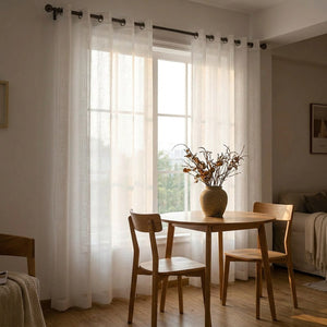 Voilage en tulle blanc à œillets dans un coin repas avec table en bois près d'une fenêtre