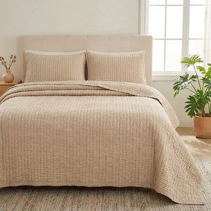 Couvre-lit matelassé beige sur un lit dans une chambre lumineuse avec une plante verte