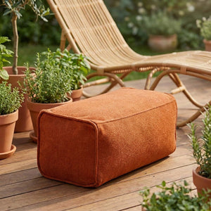 Pouf repose-pieds orange posé sur une terrasse en bois entourée de plantes