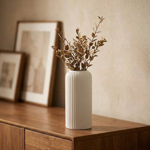 Vase blanc à rainures avec branches séchées sur un buffet en bois