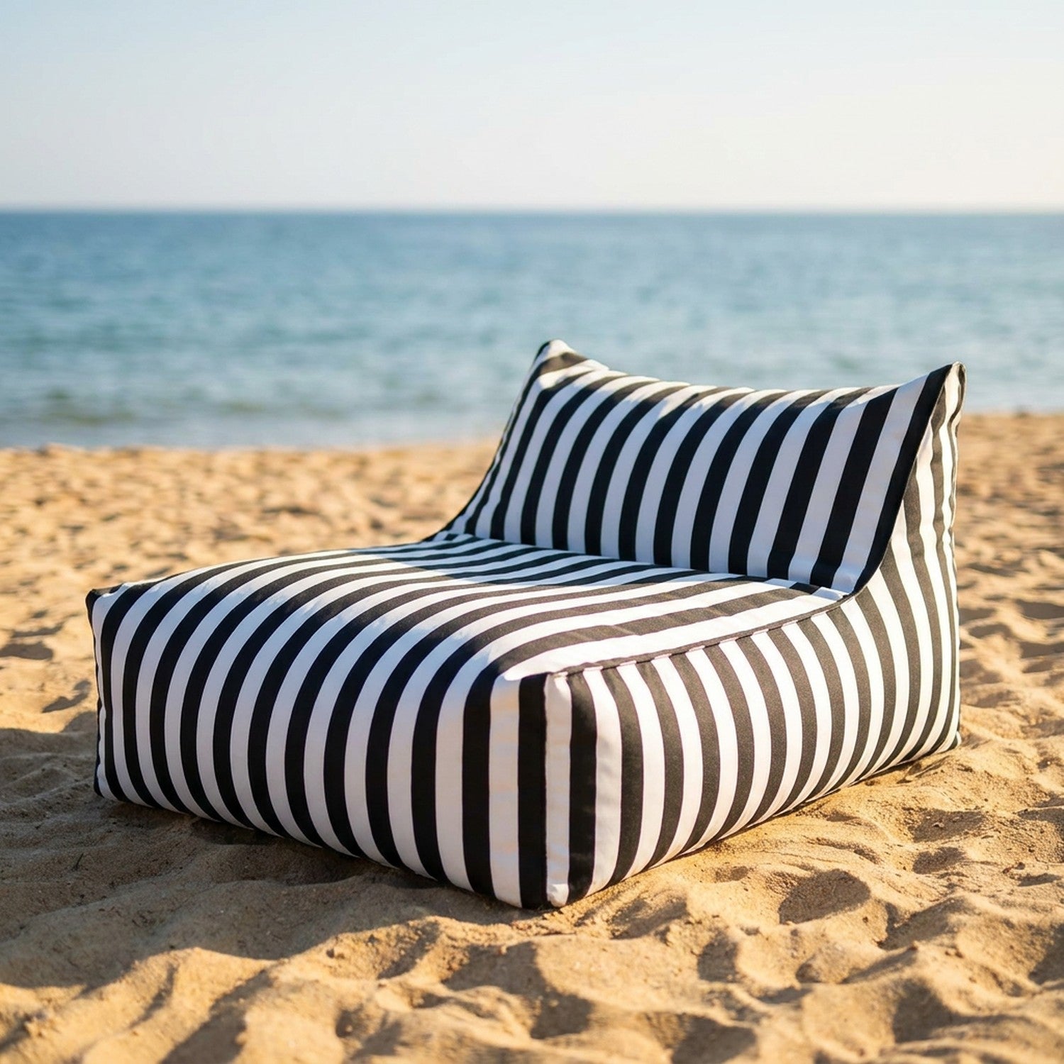 Pouf géant à rayures posé sur le sable d'une plage face à la mer