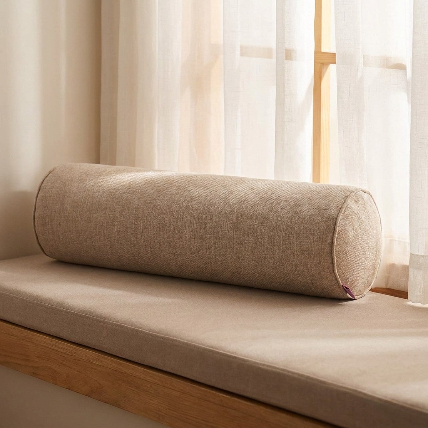 Housse de traversin cylindrique beige posée sur une banquette de fenêtre en bois