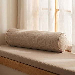 Housse de traversin cylindrique beige posée sur une banquette de fenêtre en bois