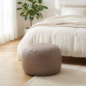Pouf en simili cuir taupe au pied d'un lit dans une chambre lumineuse