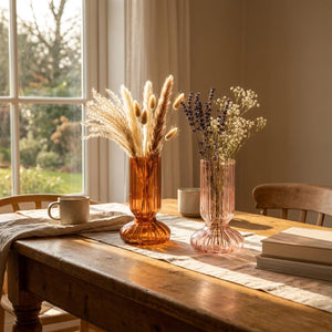 Vases en verre nervuré ambre et rose sur une table en bois à la lumière dorée
