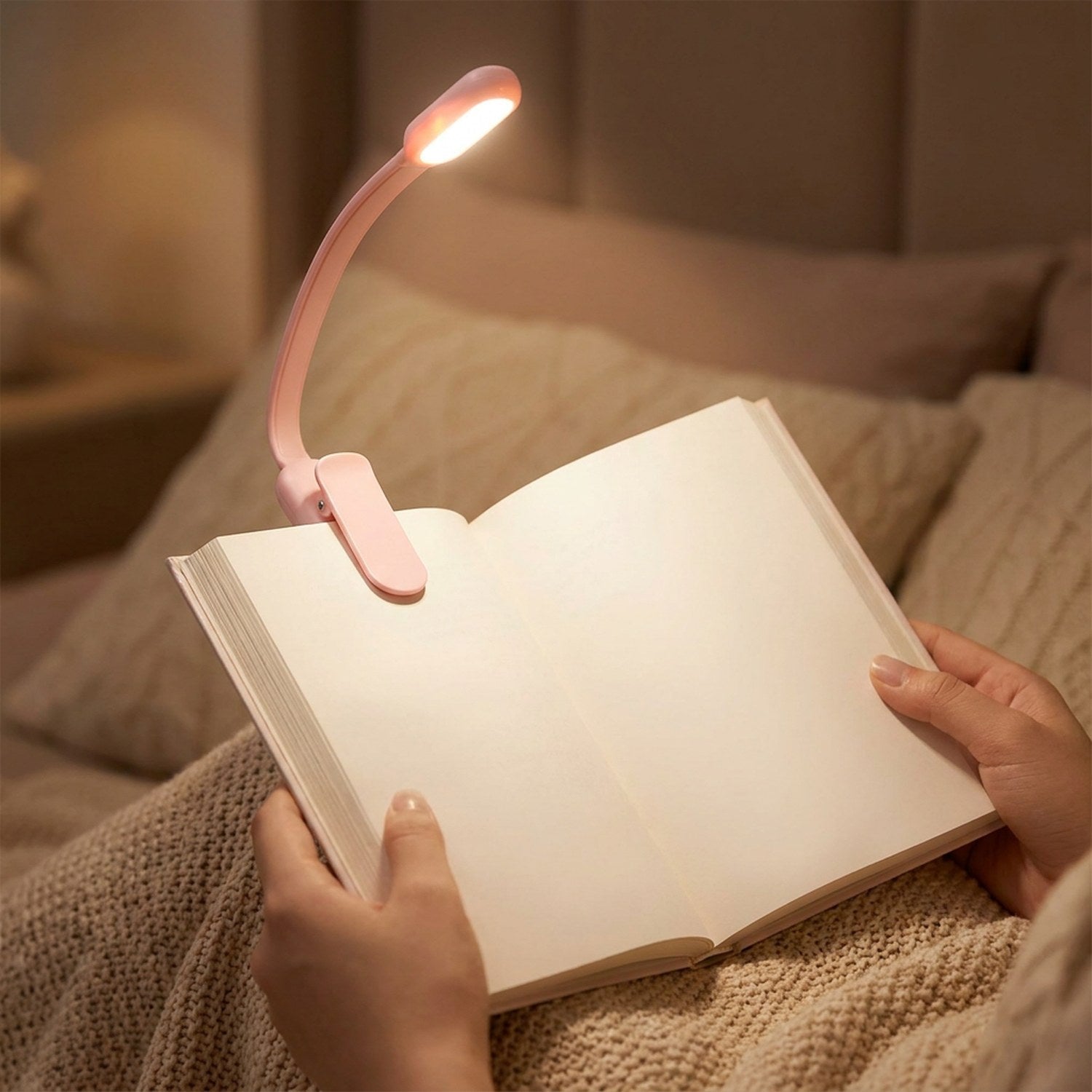Lampe de lecture à clipser rose fixée sur un livre tenu en main au lit