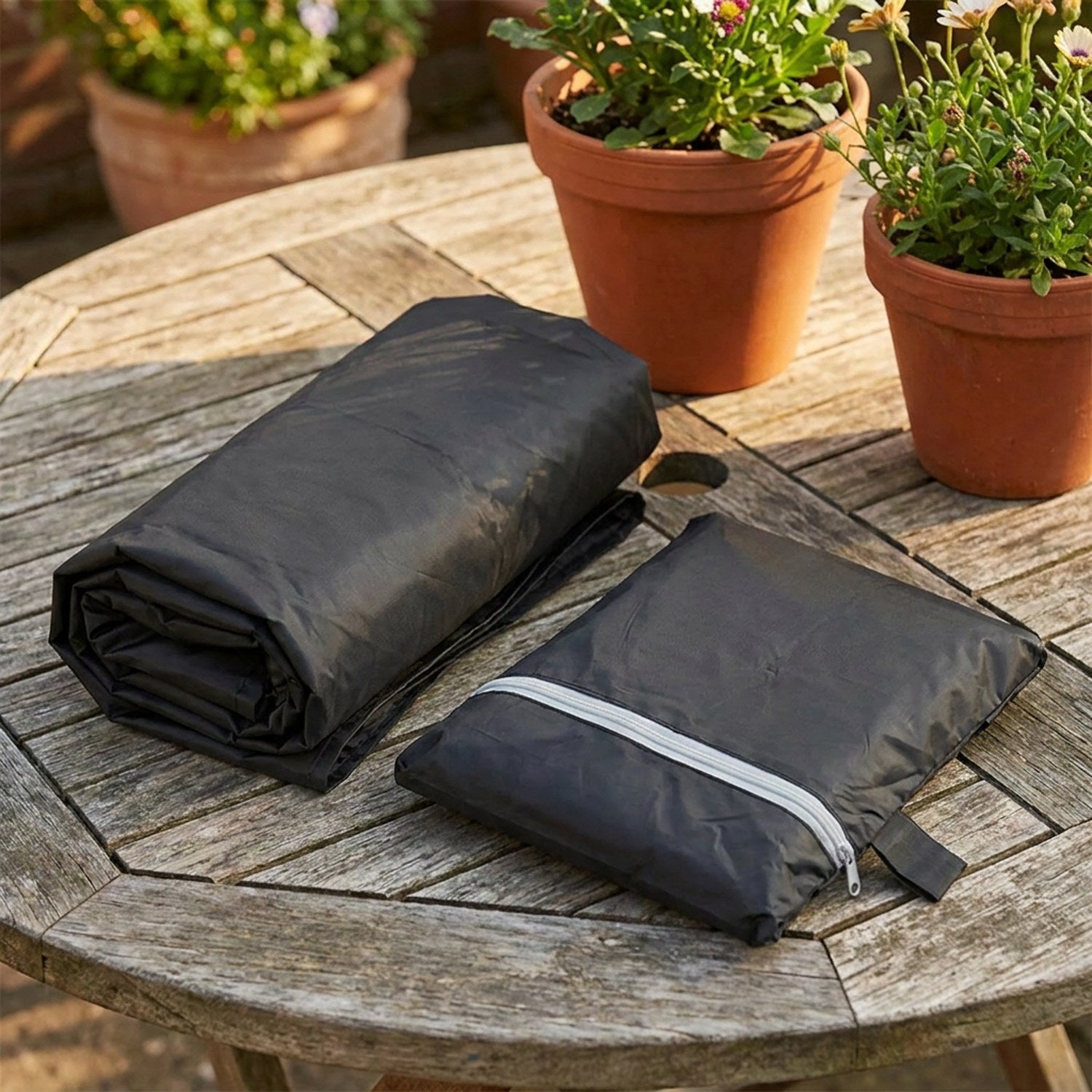 Housse de protection pliée à côté de son sac de rangement zippé sur une table de jardin