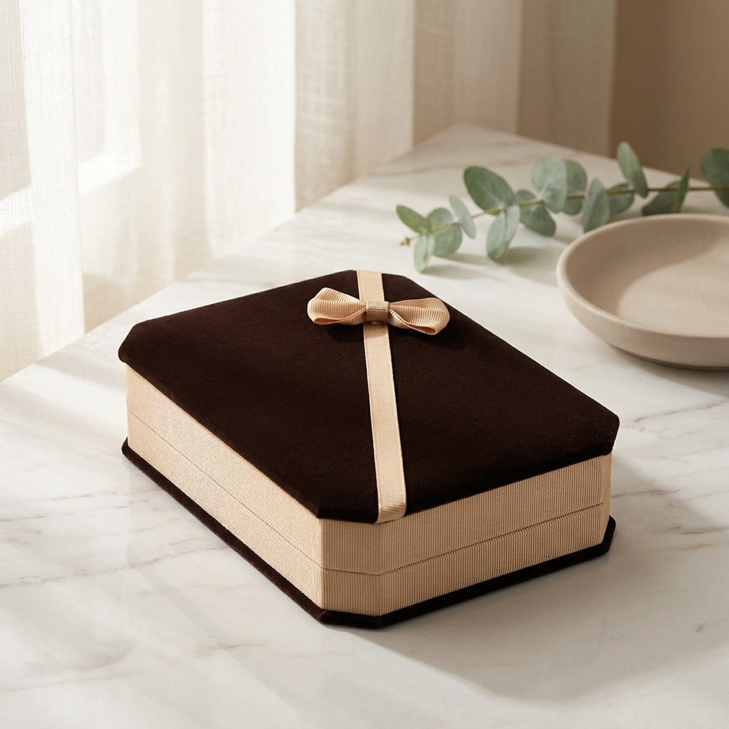 Coffret à bijoux en velours fermé posé sur un marbre près d une fenêtre avec eucalyptus